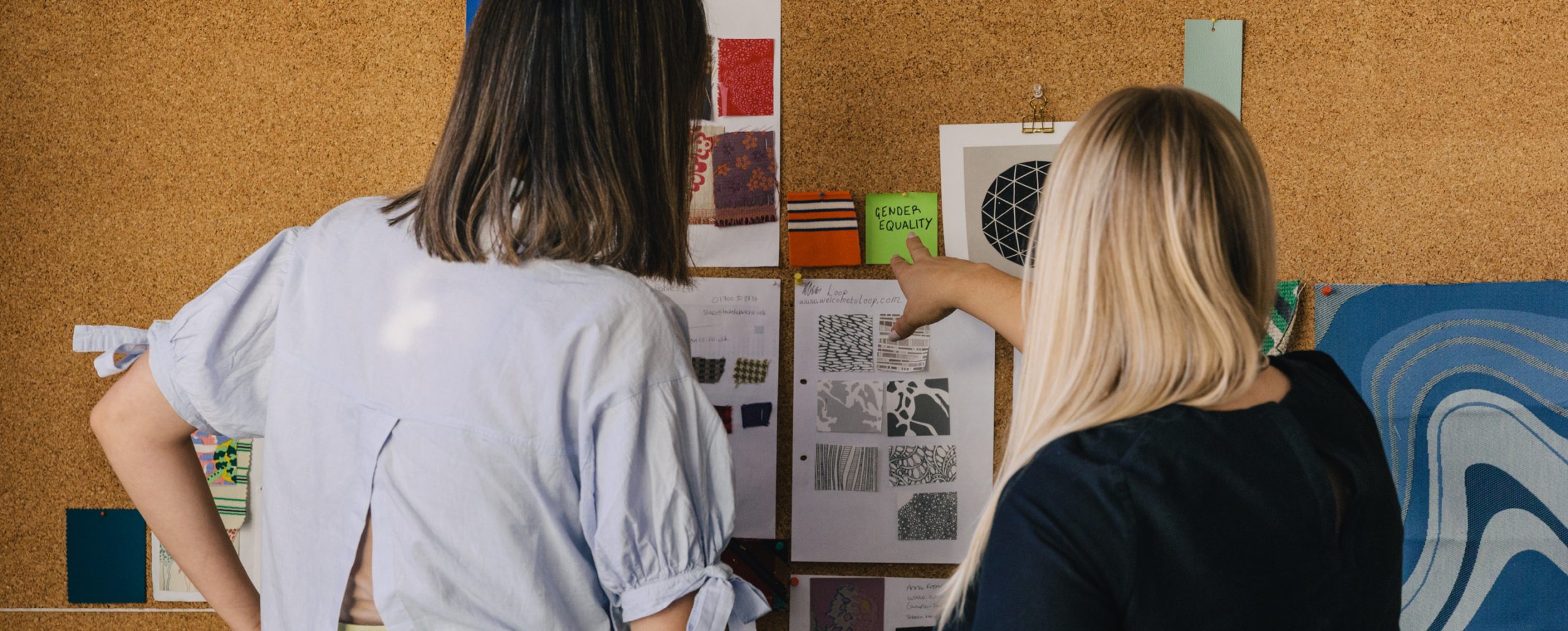 2 female trend forecasters working on a DEI forecast on a corkboard wall with fabrics and colour palettes